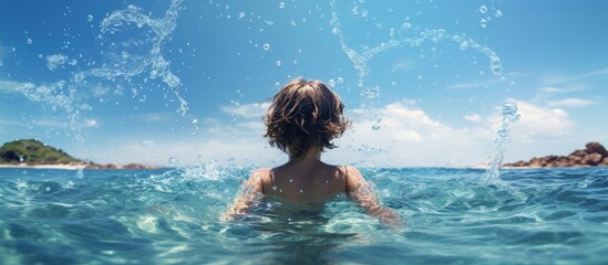 Wall Mural - A boy child playing in the sea waves enjoying the summer vacation with water splashes as seen from the back Ideal for a copy space image 167 characters