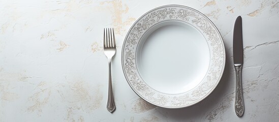 Poster - A white dinner plate sits on a white marble surface featuring intricate patterns A shiny silver spoon completes the composition The image offers ample copy space