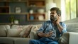 © Aamir - An Indian man sitting on a sofa in the living room holding a glass of water with neck pain