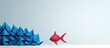 © HN Works - A red paper origami fish sits on a white background leading a group of blue origami fish The image demonstrates the concept of leadership with space available for additional content
