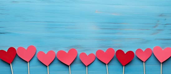 Aufkleber - A flat lay top view of a blue background with red and pink heart shaped paper cutouts attached to wooden sticks creating a Valentine s Day themed image with copy space