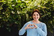 © Jacob Lund - Happy business woman showing a heart gesture while standing in a green office