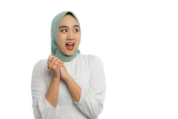 Wall Mural - Excited young Asian woman in green hijab and white blouse clasped hands and looking aside with surprised expression isolated on white background