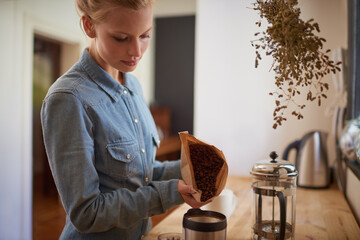 Wall Mural - Woman, coffee beans and grinder in kitchen for drink preparation with plunger for morning, caffeine or latte. Home, brown bag and pour in machine on counter for hot beverage, matcha or cappuccino