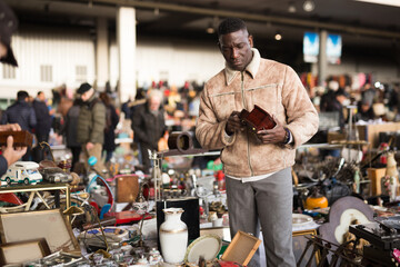 Wall Mural - Ordinary Afro-American guy considers things sacond hands on flea market