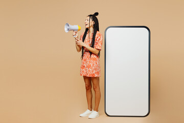 Wall Mural - Full body young Latin woman she wear orange dress casual clothes big huge blank screen mobile cell phone smartphone with area scream in megaphone isolated on plain beige background. Lifestyle concept