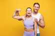 © ViDi Studio - Young cool strong fitness trainer instructor sporty two man woman wear blue clothes spend time in home gym showing biceps muscles on hand isolated on plain yellow background Workout sport fit concept