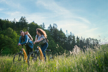 Travellers couple going on e-bike ride in nature. Tourist riding electric bicycles on easy trail road in the middle of forest. Young tourist spending summer vacation oudoors.