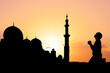 © STOCK PHOTO 4 U - Silhouette of a Person Praying at Sunset Near Mosque with Minaret in Background, Capturing Spirituality and Serenity in a Beautiful Evening Sky