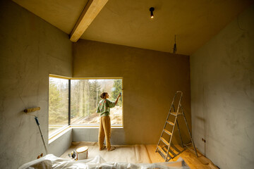 Young woman paints walls in bedroom while making repairment of a new house on nature. Creative process of home renovation and repair concept