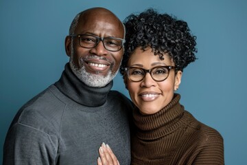 Wall Mural - Portrait of a grinning mixed race couple in their 60s wearing a classic turtleneck sweater on soft blue background