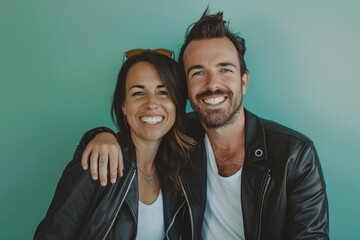 Wall Mural - Portrait of a smiling couple in their 30s sporting a stylish leather blazer in soft teal background
