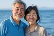 © Markus Schröder - Portrait of a glad asian couple in their 60s wearing a sporty polo shirt isolated on serene seaside background