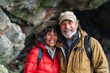 © Markus Schröder - Portrait of a grinning multicultural couple in their 60s sporting a quilted insulated jacket isolated in spectacular sea cave background