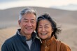 © Markus Schröder - Portrait of a glad asian couple in their 50s wearing a trendy bomber jacket while standing against serene dune landscape background