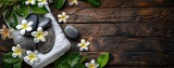 A spa setup with massage stones, a towel, and frangipani flowers on a wooden background, with ample room for text