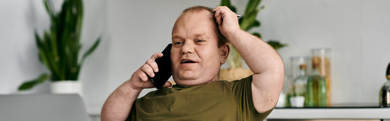 A man with inclusivity in casual attire sits at home talking on the phone.