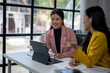 © Wasana - Two women are sitting at a table with a laptop and a tablet