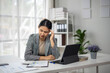 © Wasana - A woman sits at a desk with a laptop and a stack of papers