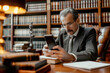 © Renata Hamuda - A male lawyer using a smartphone to talk to client and consulting work with Law book in law office