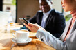 © Marko Geber - Close-up of business colleagues reviewing a smartphone in a cafe with a cup of coffee on the table