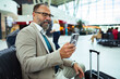 © Davor - Smiling businessman using smartphone while sitting with luggage at train station