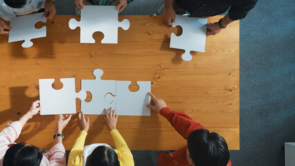 Wall Mural - Top down view of skilled business people assemble jigsaw puzzle on meeting table. Group of diverse team working together to solve the puzzle. Represented unity, togetherness, cooperative. Convocation.