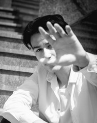 Young man, teenage model sits on steps in city, tuch, no. Casual, fashion. BW grainy photo