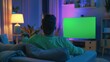 © neirfy - A man watches TV with a green screen in a modern living room, enhancing his leisure time in a cozy environment
