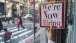 © Generative ART - Hand Placing a We're Now Hiring Sign in a Window on a Busy City Street