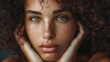 © VK Studio - A young woman with curly hair and freckles gazes intently at the camera, her hands gently framing her face, with a soft, thoughtful expression.