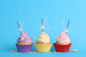 Wall Mural - Birthday cupcakes with burning sparklers and sprinkles on light blue background