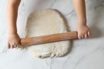 Wall Mural - Little child rolling raw dough at white table, top view