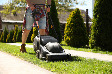 Wall Mural - Man cutting green grass with lawn mower on backyard, closeup