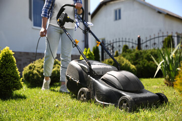 Wall Mural - Woman cutting green grass with lawn mower in garden, closeup