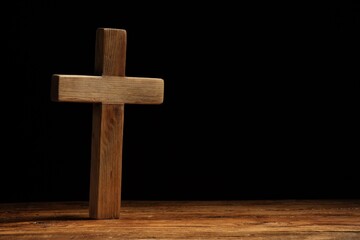 Wall Mural - Cross on wooden table against black background, space for text. Religion of Christianity