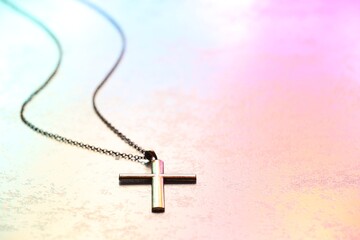 Wall Mural - Cross with chain on textured table in color lights, closeup and space for text. Religion of Christianity