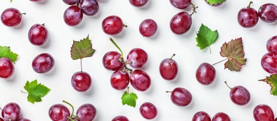 Wall Mural - Red grapes with green leaves and sliced in half are set against a white background, viewed from the top to create a flat lay. The arrangement forms a grape pattern texture background.