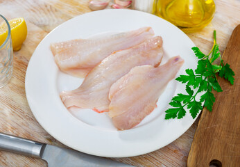 Wall Mural - Fresh raw sea bass fillet on a plate, cooked for cooking in a home kitchen with a sprig of parsley and lemon