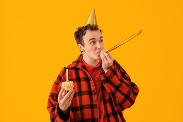 Poster - Young man with birthday cake and party whistle on yellow background