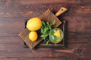 Wall Mural - Boards with glass of fresh mint tea and lemons on brown wooden background