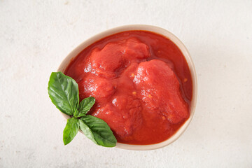 Wall Mural - Bowl of canned tomatoes with basil on light background