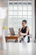 © Mongta Studio - A young professional woman working on her laptop at a modern cafe, holding a coffee cup and smiling, with a glass block wall in the background.