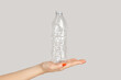 © khosrork - Closeup of woman hand holding empty plastic bottle, utilization, zero waste. Indoor studio shot isolated on gray background.