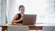 © Mongta Studio - A young woman working on her laptop in a bright home office, holding a coffee cup. Modern workspace with natural light.