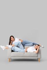 Wall Mural - Young women in stylish jeans lying on sofa against light background