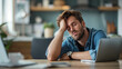 © iamfrk7 - Exhausted man resting his head on his hand while sitting in front of a laptop at home, indicating fatigue from working remotely or studying. Generative AI.