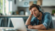 © iamfrk7 - Exhausted man resting his head on his hand while sitting in front of a laptop at home, indicating fatigue from working remotely or studying. Generative AI.