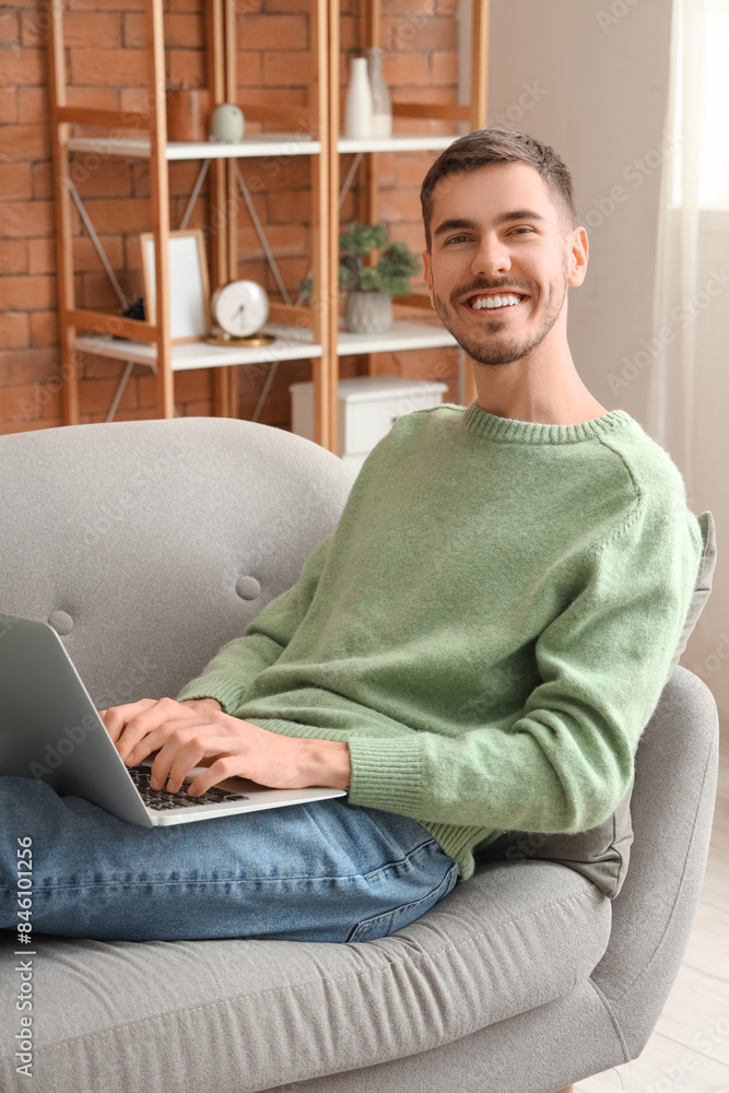Handsome young happy man with laptop resting on sofa at home