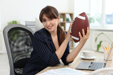 Wall Mural - Smiling employee with american football ball at table in office